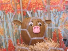 a fake cow is sitting in hay behind a fence with trees and leaves painted on it