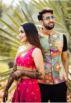 a man and woman standing next to each other in front of palm trees with henna tattoos on their arms