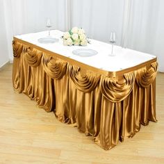 the table is covered with gold drapes and white plates on it's centerpiece