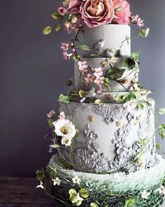 a three tiered wedding cake with flowers on top and greenery around the edges