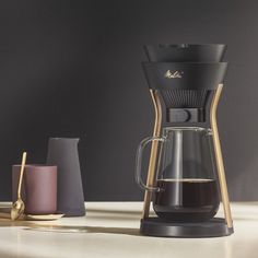 a coffee maker sitting on top of a counter next to two cups and a mug