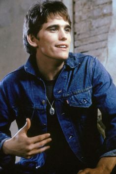 a young man sitting down with his hands in his pockets and wearing a denim jacket