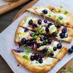 a pizza topped with blueberries and cheese on top of a wooden cutting board next to bread