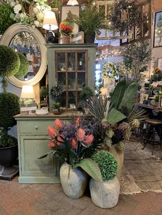 a room filled with lots of potted plants next to a dresser and mirror on the wall