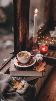 a cup of coffee sitting on top of a stack of books next to a candle