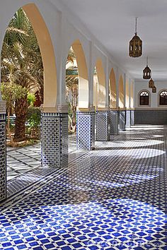 an empty hallway with blue and white tiles on the floor, surrounded by palm trees