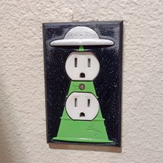 a green and white light switch cover with an alien hat on it's head