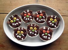 cupcakes with chocolate frosting decorated as monsters on a white plate and wooden table