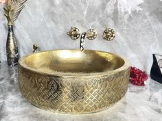 a gold bathroom sink sitting on top of a counter next to a vase with flowers