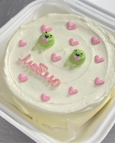 a white cake with pink and green decorations in a plastic container