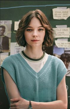 a woman with her arms crossed standing in front of a chalkboard covered bulletin board