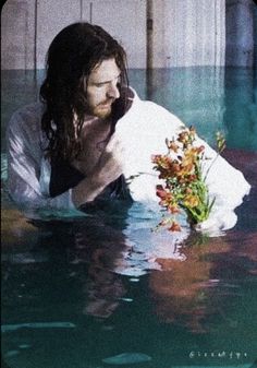 a man with long hair holding flowers in the water