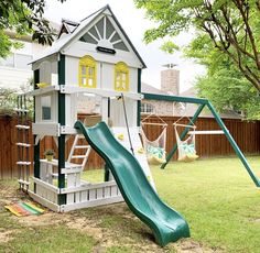 a play set in the backyard with a green slide and white house on it's side