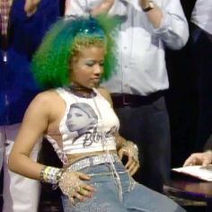 a woman with green hair sitting at a table in front of other people and talking on the phone