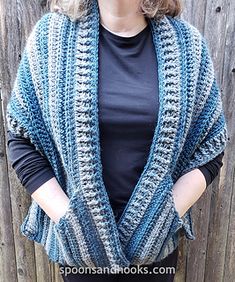 a woman standing in front of a wooden fence wearing a blue and white crocheted shawl