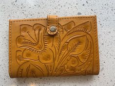 Each beautiful Alexis David creation is of the highest quality hand-tooled, hand-dyed leather, uniquely crafted and hand laced in a variety of gorgeously deep, rich colors to suit every mood and every season! The embossed hand-tooling is deep and detailed in intricate designs that suit the particular style of each bag. PLEASE ALLOW 6-8 WEEKS FOR ALL COLORS TO SHIP Leather Magnetic snap closure 6 credit card slots Inside zipper pocket for coins Check book compartment if needed Suede lining Sturdy Artisan Hand-tooled Wallets For Everyday Use, Artisan Hand-tooled Wallets For Daily Use, Artisan Hand Tooled Wallet For Everyday Use, Artisan Hand Tooled Leather Wallet, Traditional Hand Tooled Wallets For Everyday Use, Artisan Hand Tooled Wallets, Tooled Leather Wallet, Check Book, Leather Passport Cover