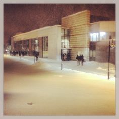 people are walking in the snow outside of a building at night with no one on it