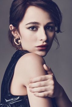 a woman in black dress posing with her arm around her shoulder and wearing large gold hoop earrings