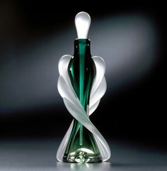 a green and white glass vase sitting on top of a black table next to a wall