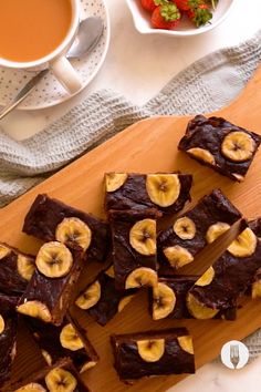 chocolate brownies with banana slices and strawberries on a wooden cutting board next to a cup of tea