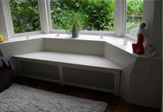 a corner bench in front of a window with plants on the windowsill and rugs around it