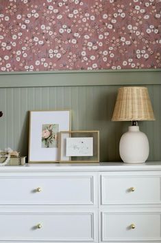 a white dresser topped with lots of drawers under a pink flowered wallpaper covered in flowers