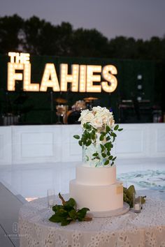 AlphaLit Marquee Letter Lights spell out "The Flahies' behind the wedding band stage. The stage is next to the dance floor, and the wedding cake sits on a table on the dance floor. The cake is circular with three levels, the top layer covered in a bouquet of white roses with greenery cascading down the sides. Lights For Wedding, Wedding Dance Floor, Letter Lights, Lighted Marquee Letters, Dance Floor Wedding, Wedding Dance