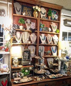 a display case filled with lots of necklaces and bracelets on wooden shelves next to a lamp