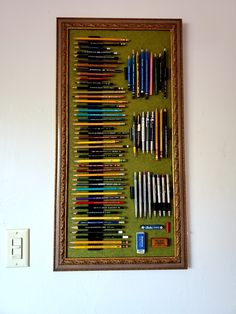 there are many different colored pencils in the frame on the wall next to an electrical outlet