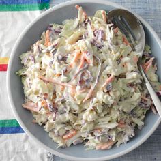 a white bowl filled with coleslaw on top of a striped table cloth next to a fork