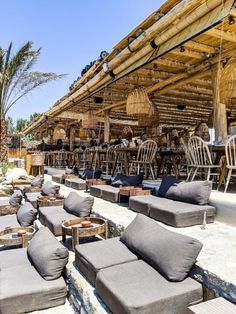 an outdoor seating area with lots of cushions and wooden tables in the background, surrounded by palm trees