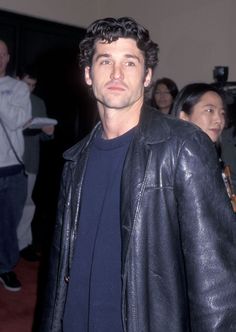 a man wearing a black leather jacket and blue shirt standing in front of a group of people