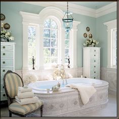 a bathroom with a large tub in the center and two windows on both sides, along with striped chairs