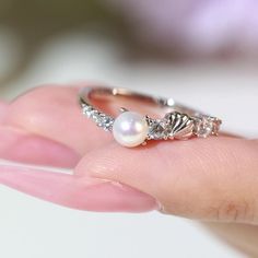 a woman's hand holding a pearl and diamond ring