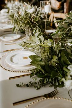 the table is set with white plates and greenery