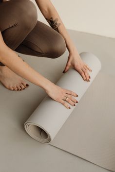 a woman in tights is rolling up a yoga mat with her hands on it