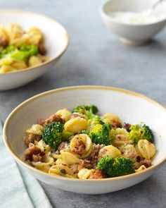 two bowls filled with pasta and broccoli on top of a gray tablecloth