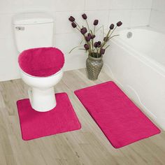 a white toilet sitting next to a bath tub filled with pink rugs on top of a wooden floor