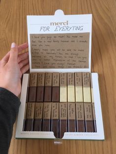 a person holding a box of chocolates on top of a wooden table with writing in it