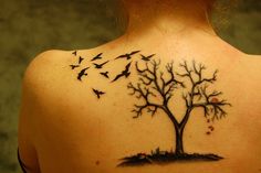 a woman's back with a tree and birds tattoo on it