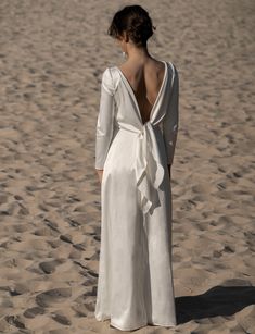 a woman standing in the sand wearing a white dress with a backless neckline