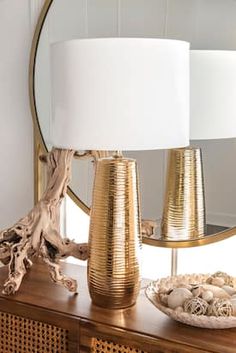 a gold lamp sitting on top of a wooden table next to a mirror and bowl