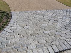 a brick walkway in front of a house with grass and bushes on the other side