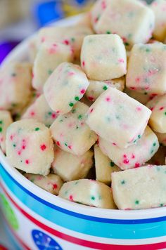 a white bowl filled with christmas sprinkles and sugar cube cookies on top of a blue striped table cloth