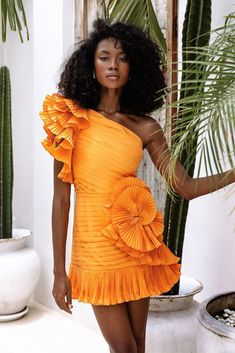 a woman in an orange dress standing next to a potted plant and palm tree