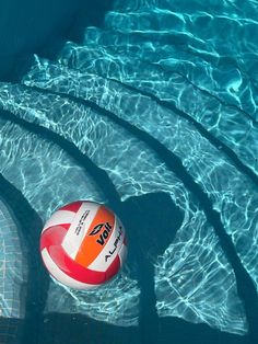 an orange and white beach ball sitting in the middle of a pool with clear blue water