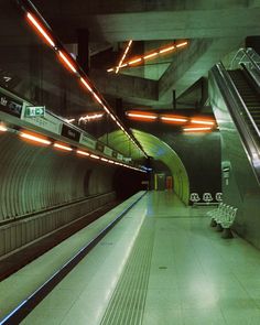 an escalator in a subway station with lights on the ceiling and two benches next to it