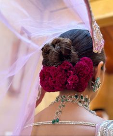 a woman with flowers in her hair wearing a pink veil over her head and jewelry on her neck