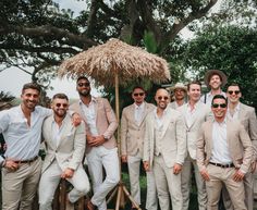 a group of men standing next to each other in front of a tree with an umbrella