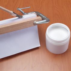 a white cup sitting on top of a wooden table next to a hammer